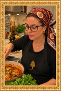 Cooking lifestyle image wearing the black Saudades Sempre apron in the gold frame